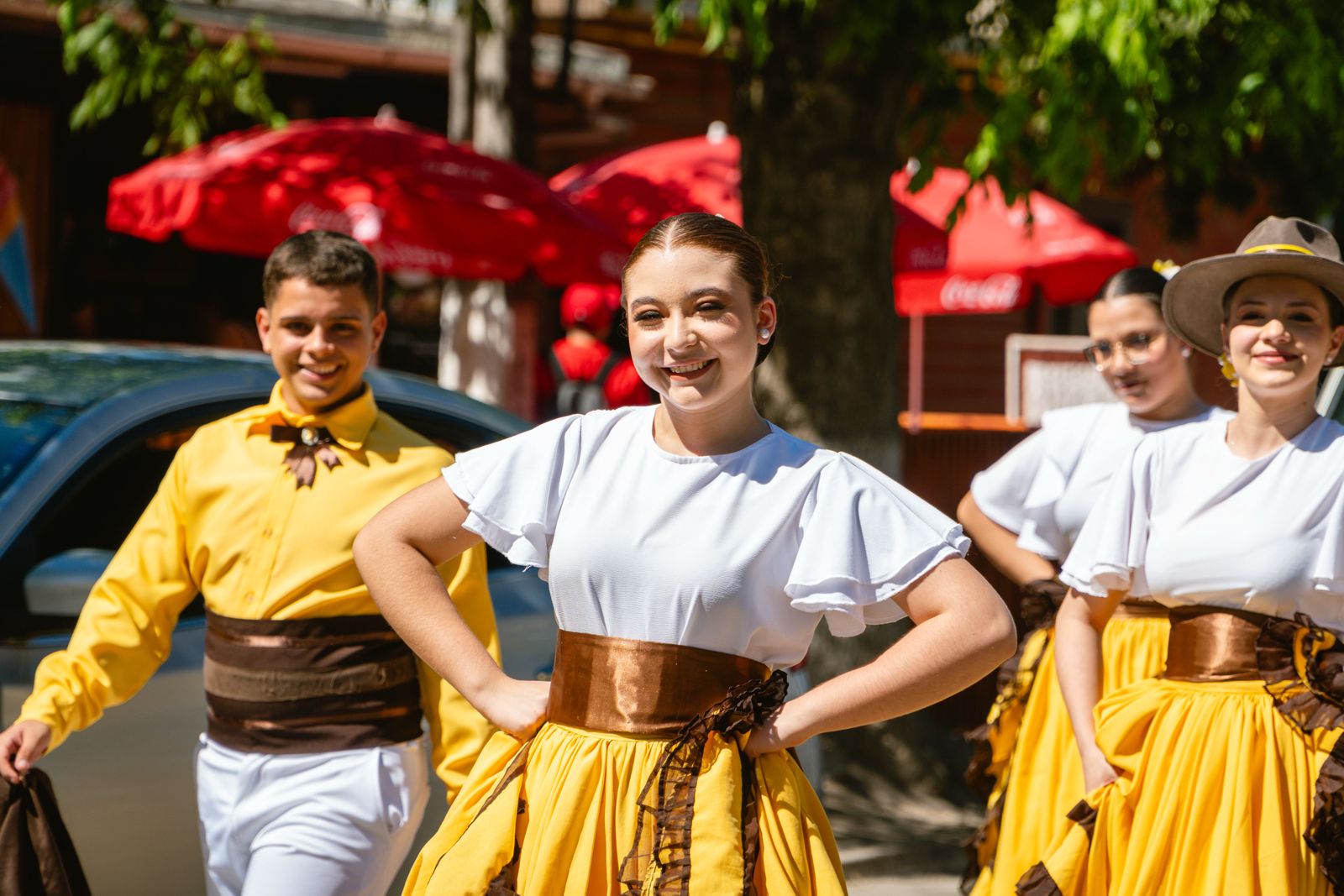 Jóvenes bailarines con trajes amarillos y blancos sonriendo en el pasacalle